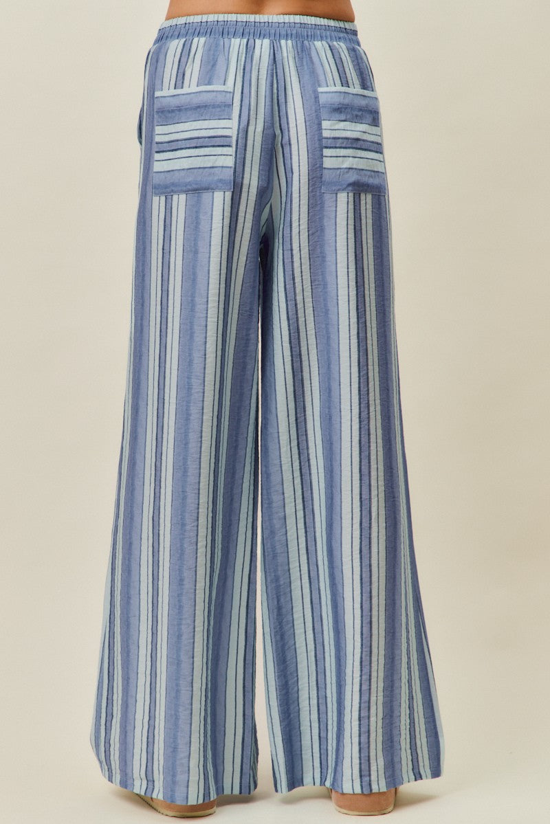 A pair of women's high-waisted wide-leg pull-on pants featuring vertical stripes in shades of blue with a gathered elastic drawstring waistband and side pockets.