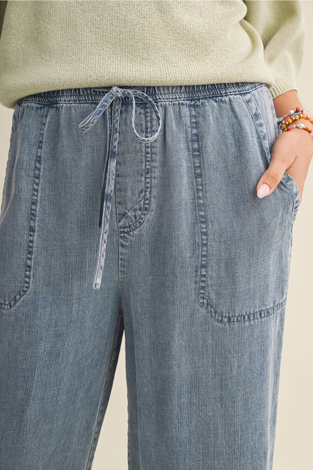 A pair of women's high-waisted wide-leg denim chambray pants featuring a gathered elastic drawstring waistband and functional front patch pockets.