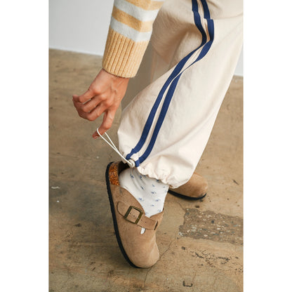 A pair of women's wide-leg relaxed cream track pants featuring double navy blue side stripes, an elastic drawstring waistband, and a mid-rise fit.