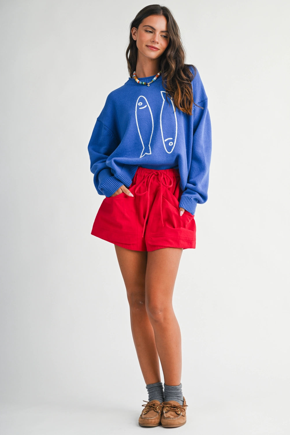 A women's royal blue long-sleeve knit crewneck sweater featuring a white embroidered sardine graphic on the front and ribbed trim along the collar, cuffs, and hem.
