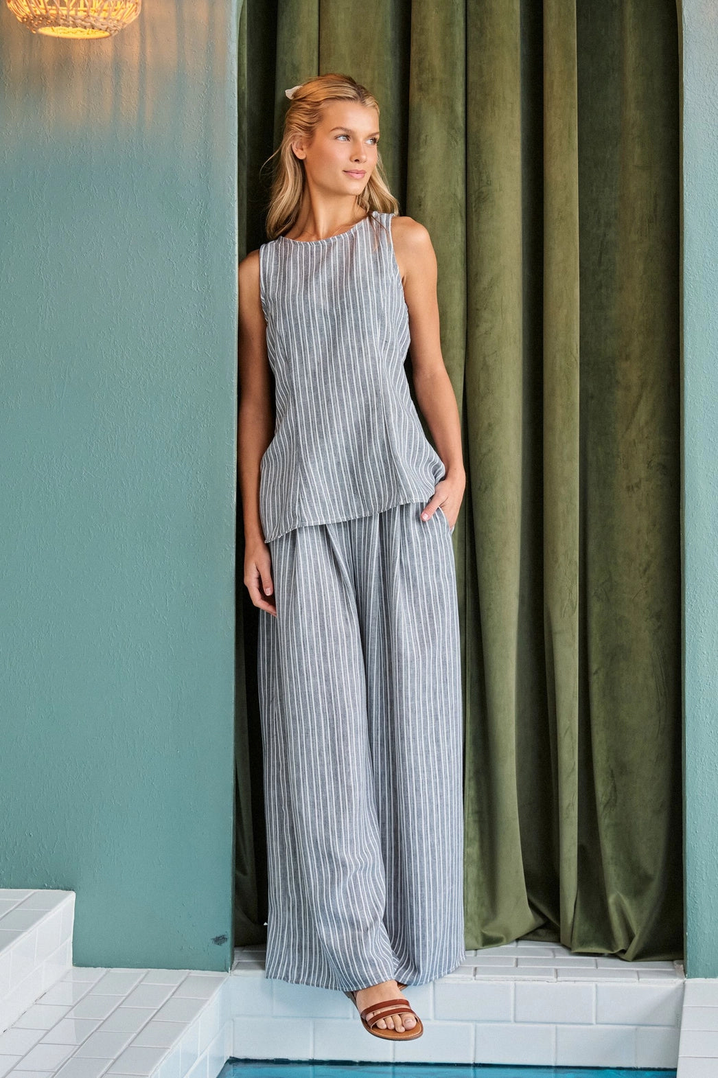 A women's two-piece pinstripe clothing set in a muted gray and white color-way featuring a sleeveless high-neck tunic top and matching high-waisted flowing wide-leg pants with side pockets.