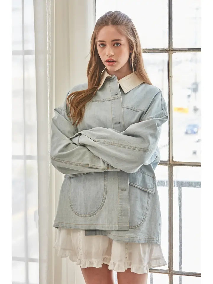 A women's relaxed oversized light wash denim utility jacket featuring a cream-colored pointed contrast collar, a button-front closure, and large front patch pockets with flaps.