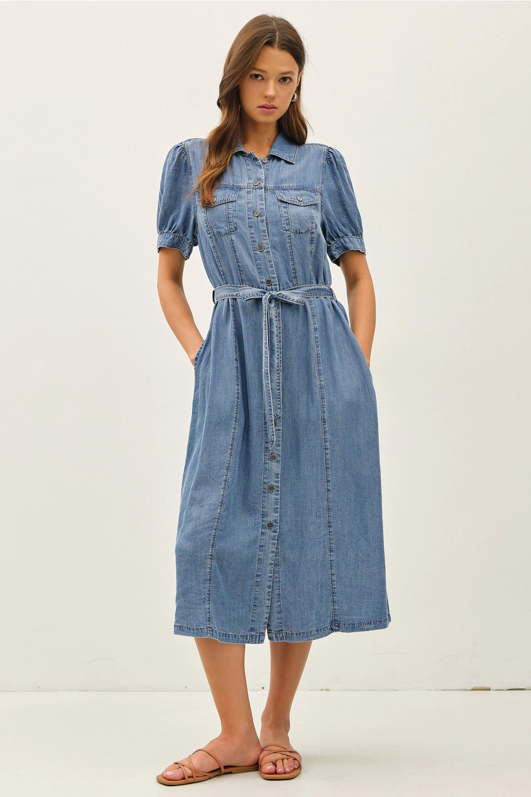 A women's short puff-sleeve denim shirt dress in a light wash featuring a pointed collar, a full button-down front, a matching waist tie belt, and convenient side pockets.