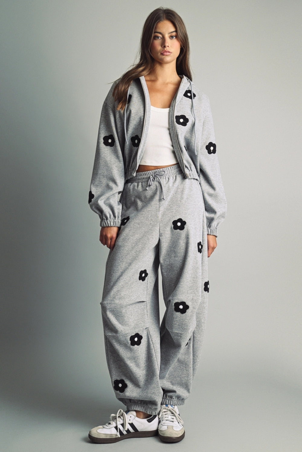 A women's heather gray full-zip hooded fleece jacket featuring dropped shoulders, ribbed hem cuffs, and black chenille flower patches on the front and sleeves.