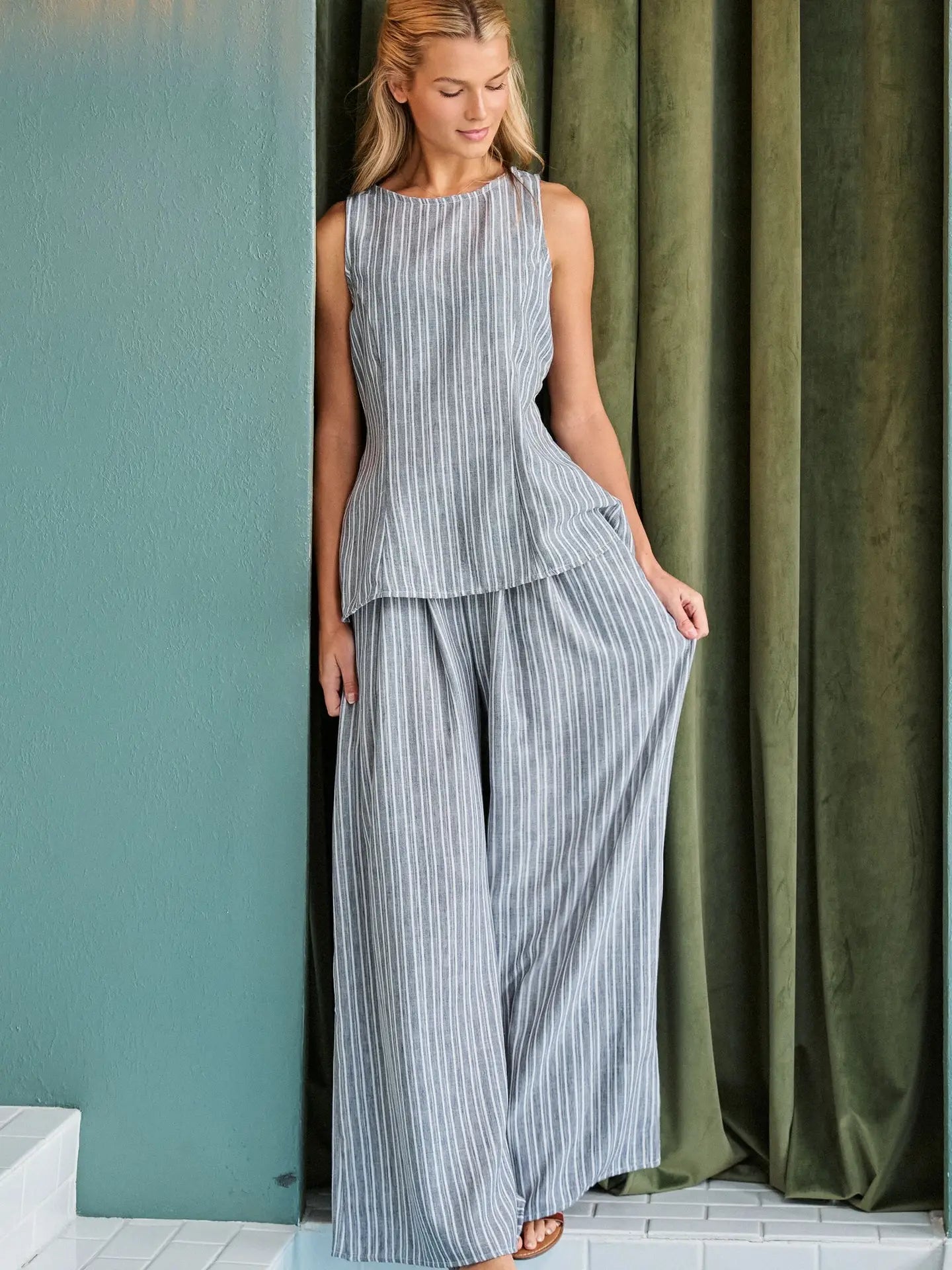 A women's two-piece pinstripe clothing set in a muted gray and white color-way featuring a sleeveless high-neck tunic top and matching high-waisted flowing wide-leg pants with side pockets.