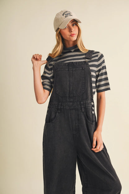 A pair of women's high-waisted wide-leg twill overalls in a vintage washed black denim finish featuring classic adjustable shoulder straps, a front chest pocket, and side pockets.