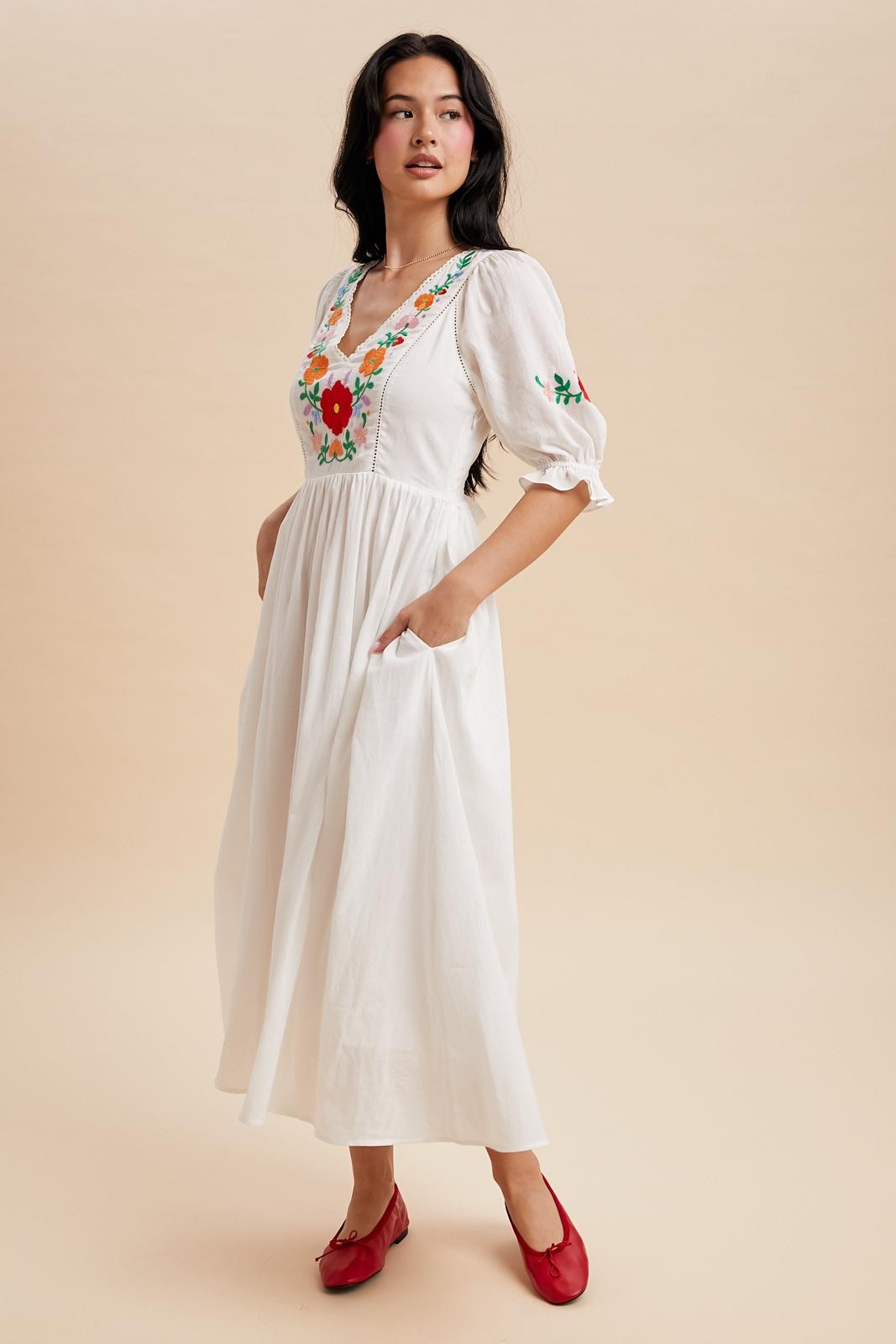 Off white maxi dress with a v-neck and embroidered bodice.  The sleeves are cuffed with a ruffle detail and hit just above the elbow with minimal embroidered detail. Waist tie in the back. 