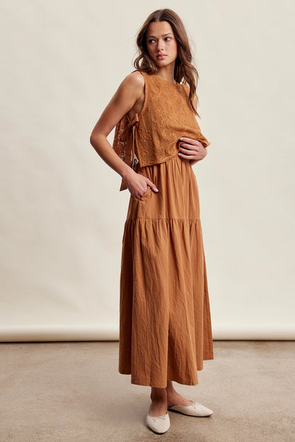 A women's brown sleeveless tiered maxi dress featuring a tonal embroidered floral lace vest overlay with adjustable side tie details.