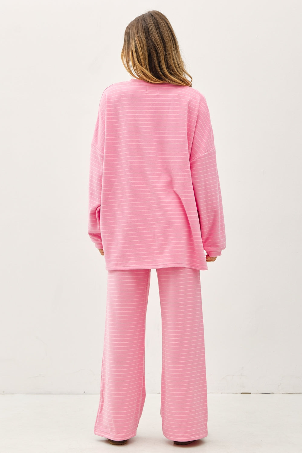 A women's relaxed long-sleeve crewneck top in bubblegum pink with ivory horizontal micro-stripes, dropped shoulders, and subtle side hem vents.