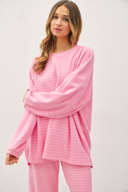 A women's relaxed long-sleeve crewneck top in bubblegum pink with ivory horizontal micro-stripes, dropped shoulders, and subtle side hem vents.