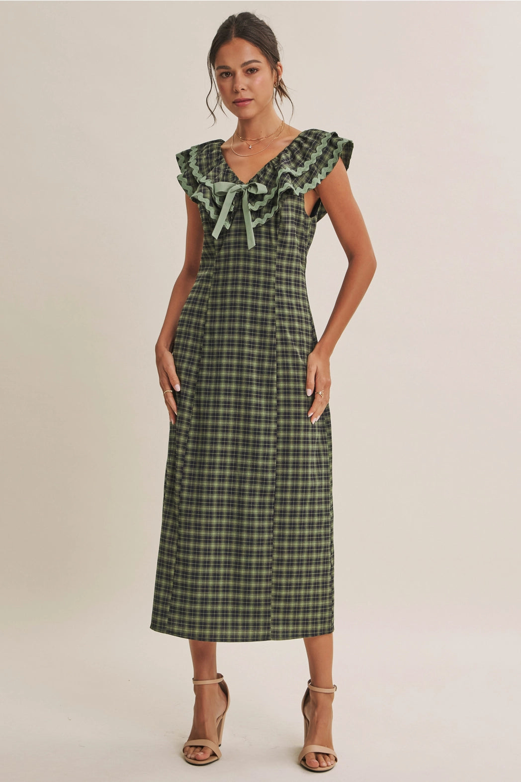 A women's ruffle midi dress featuring an evergreen and navy plaid pattern, a double-ruffle v-neck collar with sage green ric rac trim, a front bow tie, and a side skirt slit.
