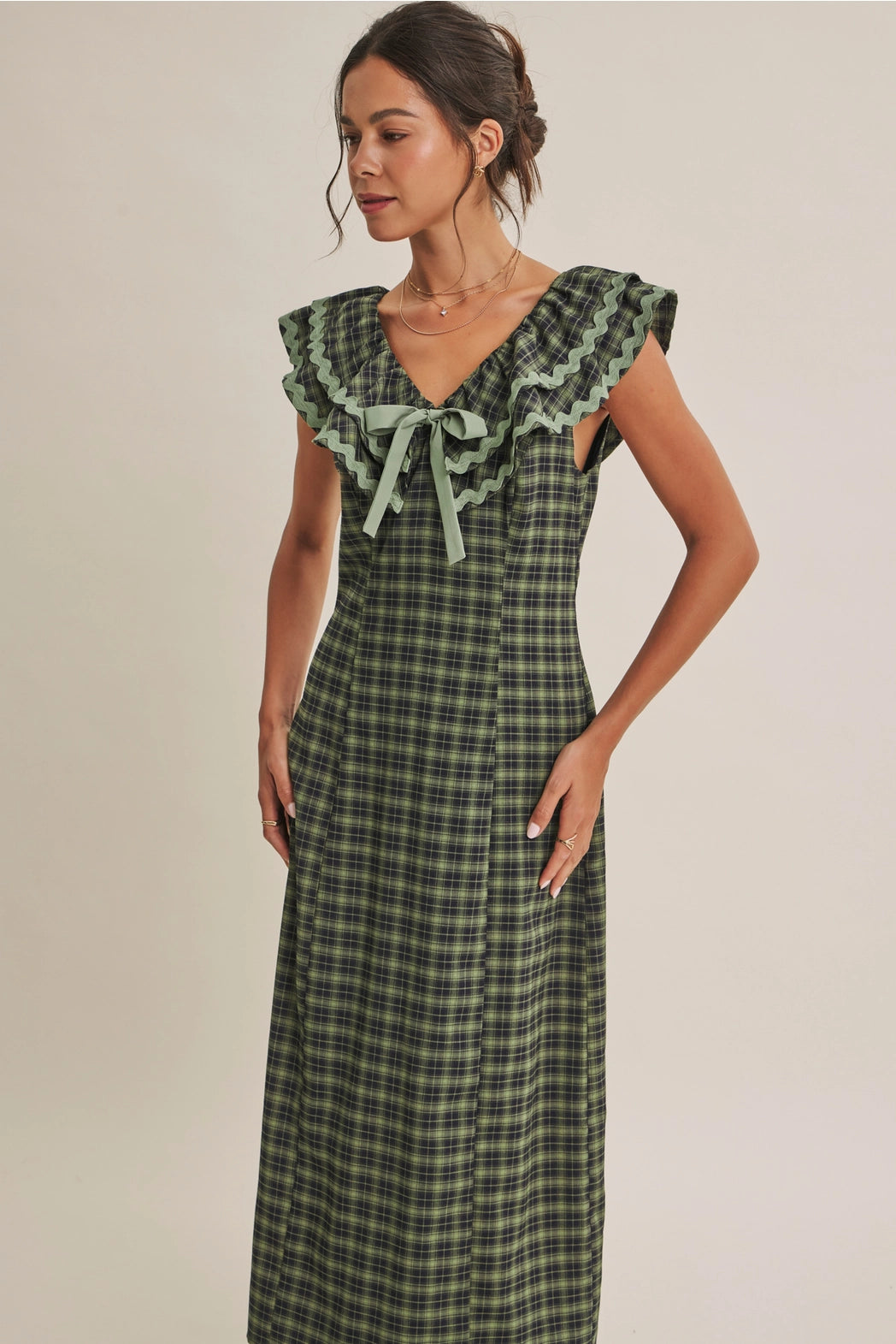 A women's ruffle midi dress featuring an evergreen and navy plaid pattern, a double-ruffle v-neck collar with sage green ric rac trim, a front bow tie, and a side skirt slit.