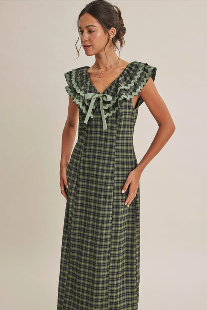 A women's ruffle midi dress featuring an evergreen and navy plaid pattern, a double-ruffle v-neck collar with sage green ric rac trim, a front bow tie, and a side skirt slit.