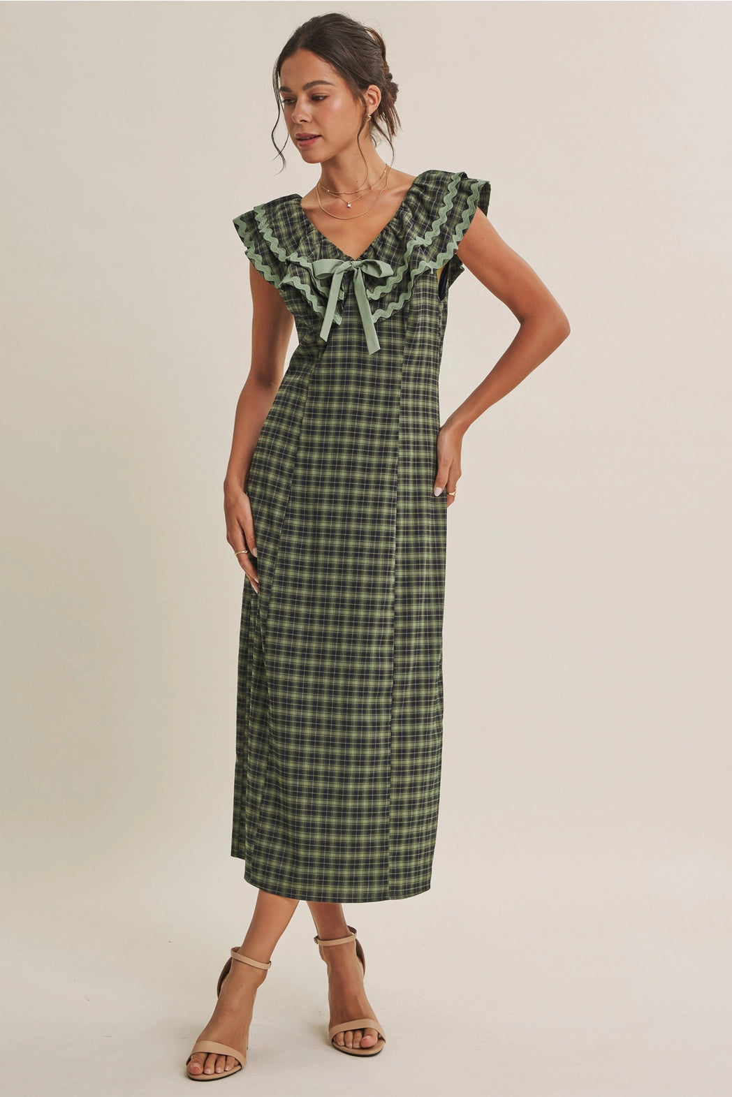 A women's ruffle midi dress featuring an evergreen and navy plaid pattern, a double-ruffle v-neck collar with sage green ric rac trim, a front bow tie, and a side skirt slit.