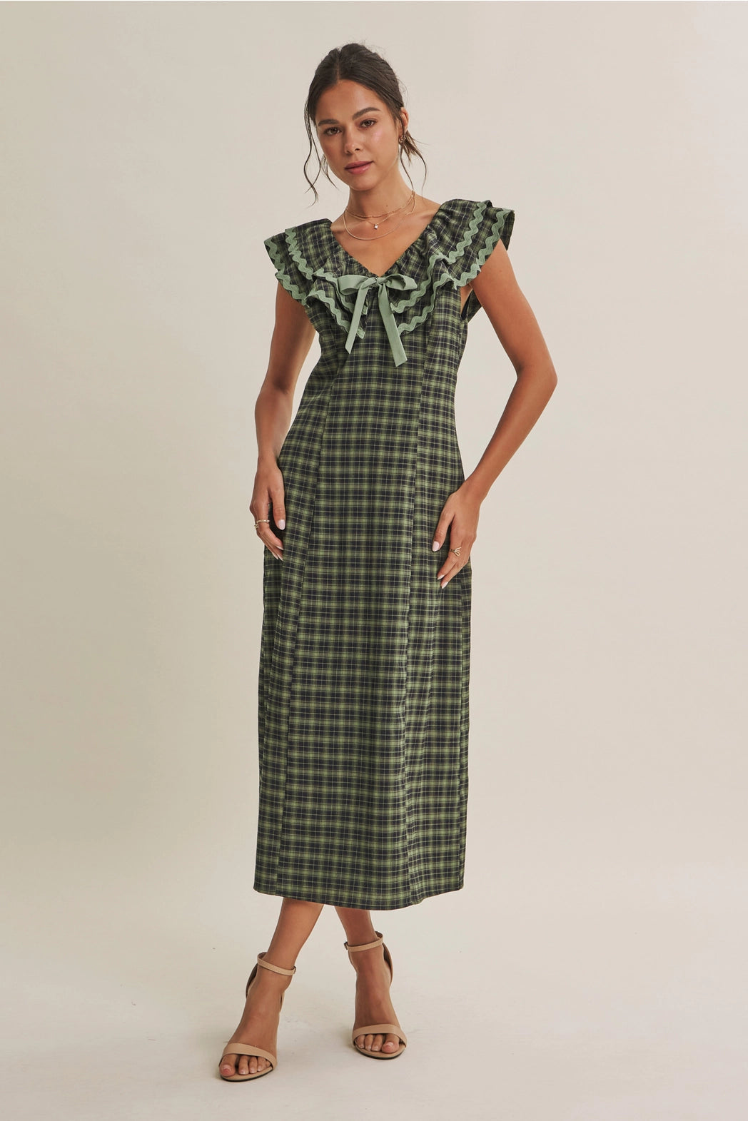 A women's ruffle midi dress featuring an evergreen and navy plaid pattern, a double-ruffle v-neck collar with sage green ric rac trim, a front bow tie, and a side skirt slit.