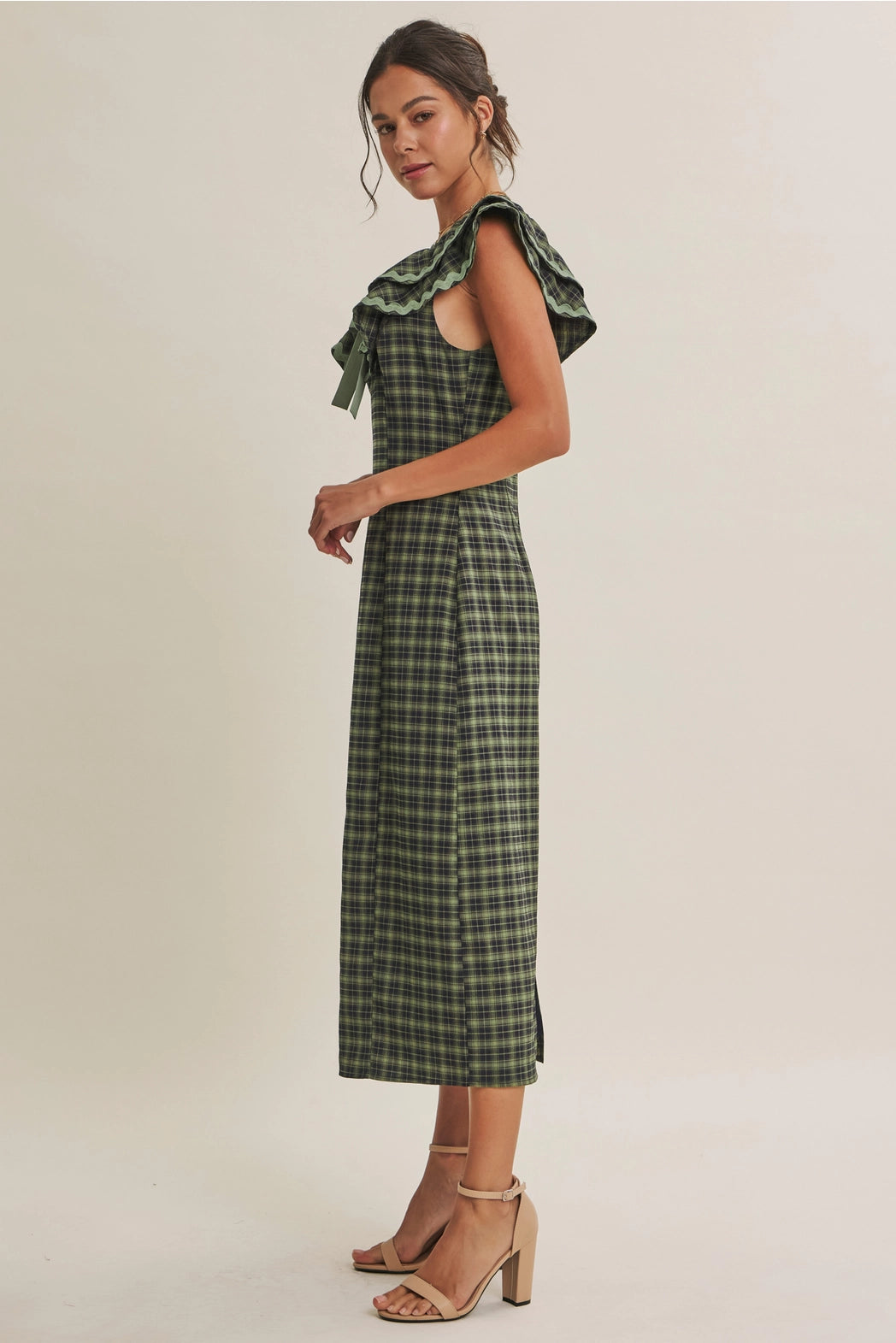 A women's ruffle midi dress featuring an evergreen and navy plaid pattern, a double-ruffle v-neck collar with sage green ric rac trim, a front bow tie, and a side skirt slit.