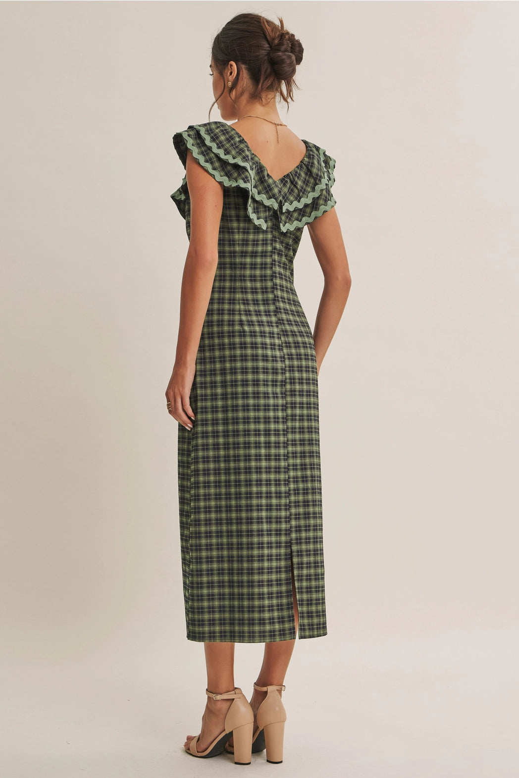 A women's ruffle midi dress featuring an evergreen and navy plaid pattern, a double-ruffle v-neck collar with sage green ric rac trim, a front bow tie, and a side skirt slit.
