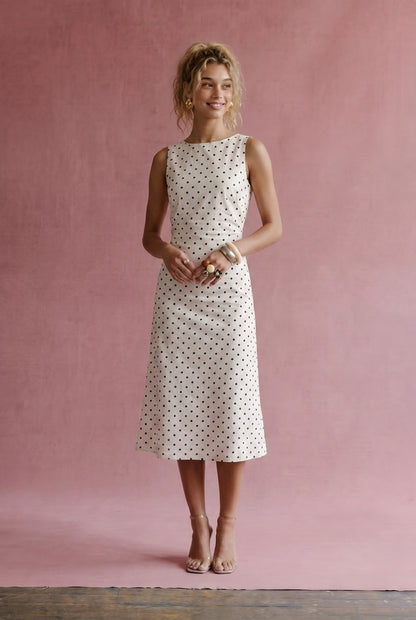 A women's sleeveless cream midi dress featuring a classic black polka dot pattern, a modest boat neckline, and an A-line silhouette.