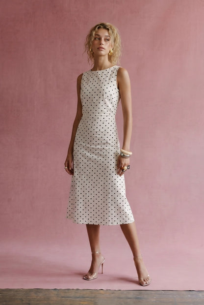 A women's sleeveless cream midi dress featuring a classic black polka dot pattern, a modest boat neckline, and an A-line silhouette.