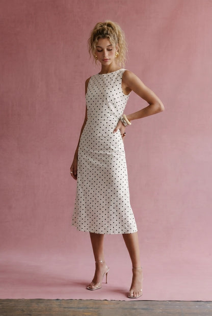 A women's sleeveless cream midi dress featuring a classic black polka dot pattern, a modest boat neckline, and an A-line silhouette.
