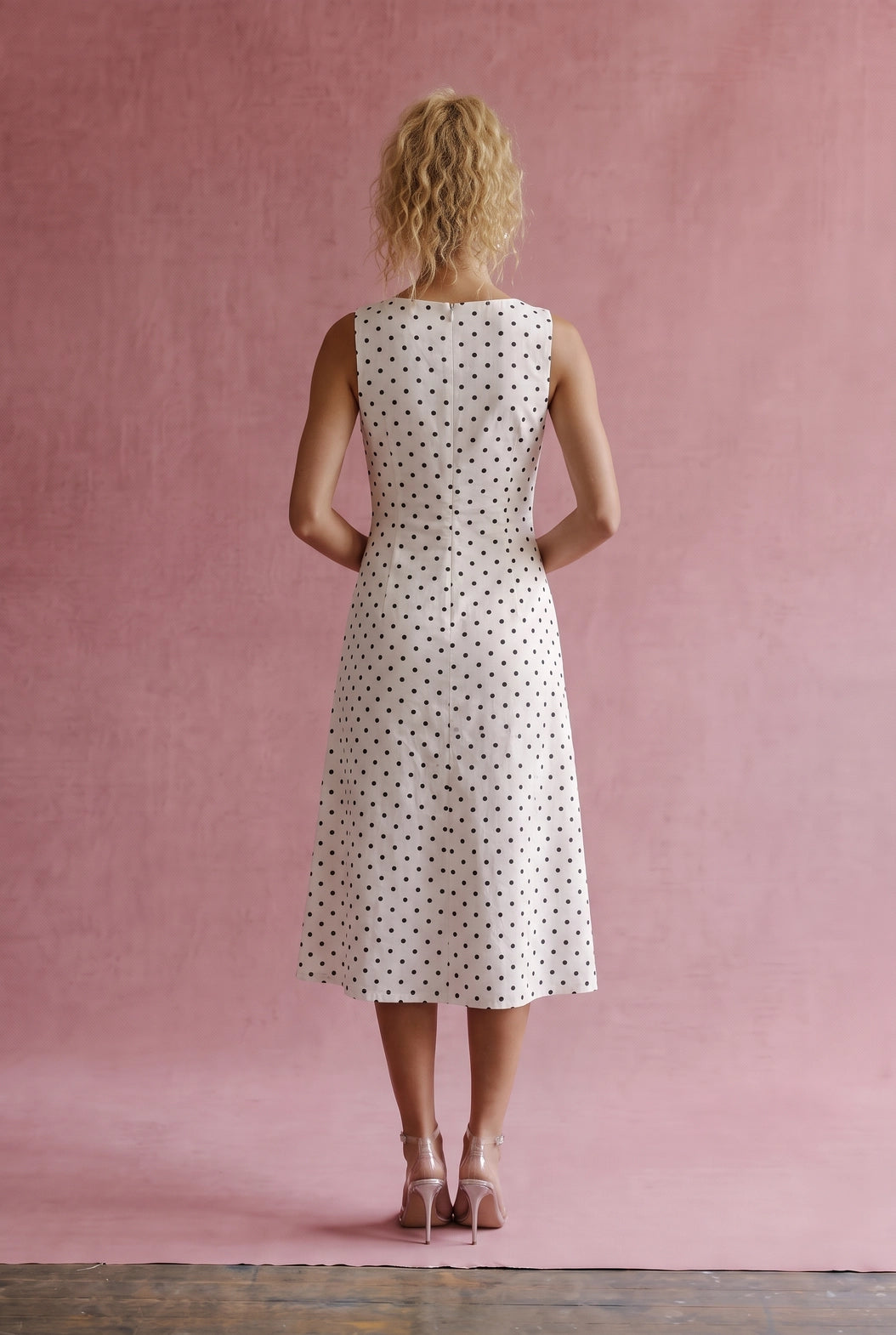A women's sleeveless cream midi dress featuring a classic black polka dot pattern, a modest boat neckline, and an A-line silhouette.