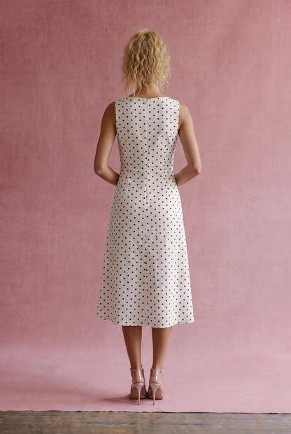 A women's sleeveless cream midi dress featuring a classic black polka dot pattern, a modest boat neckline, and an A-line silhouette.