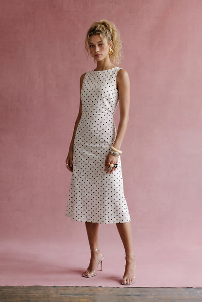 A women's sleeveless cream midi dress featuring a classic black polka dot pattern, a modest boat neckline, and an A-line silhouette.