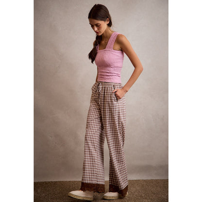 A pair of women's relaxed wide-leg brown and cream plaid pull-on pants featuring an elastic drawstring waist, side pockets, and an embroidered brown eyelet lace scalloped hem.