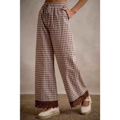 A pair of women's relaxed wide-leg brown and cream plaid pull-on pants featuring an elastic drawstring waist, side pockets, and an embroidered brown eyelet lace scalloped hem.