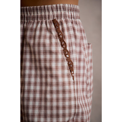 A pair of women's relaxed wide-leg brown and cream plaid pull-on pants featuring an elastic drawstring waist, side pockets, and an embroidered brown eyelet lace scalloped hem.