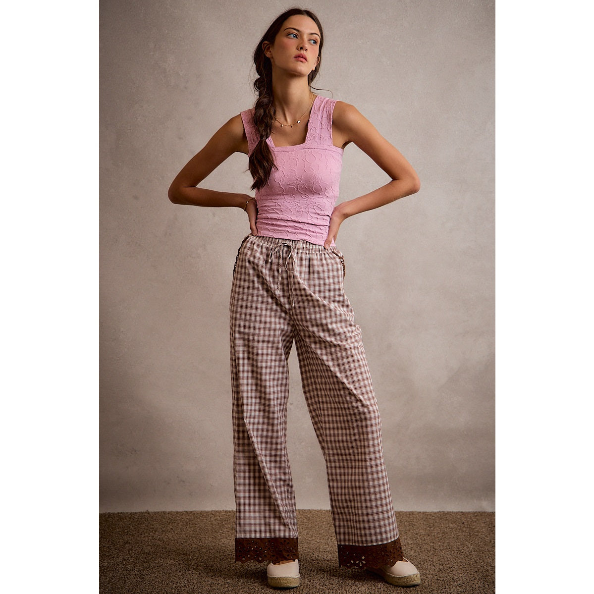 A pair of women's relaxed wide-leg brown and cream plaid pull-on pants featuring an elastic drawstring waist, side pockets, and an embroidered brown eyelet lace scalloped hem.