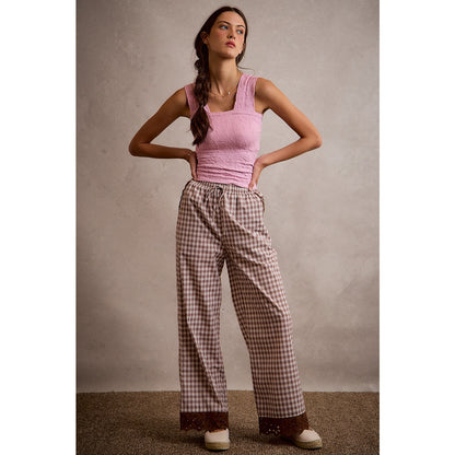 A pair of women's relaxed wide-leg brown and cream plaid pull-on pants featuring an elastic drawstring waist, side pockets, and an embroidered brown eyelet lace scalloped hem.