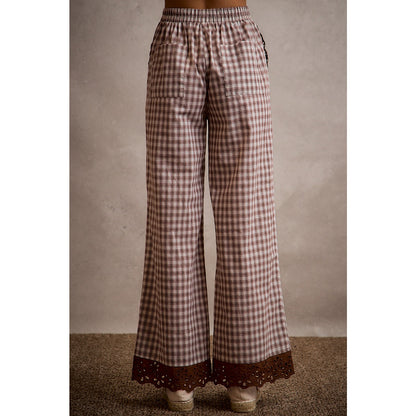 A pair of women's relaxed wide-leg brown and cream plaid pull-on pants featuring an elastic drawstring waist, side pockets, and an embroidered brown eyelet lace scalloped hem.