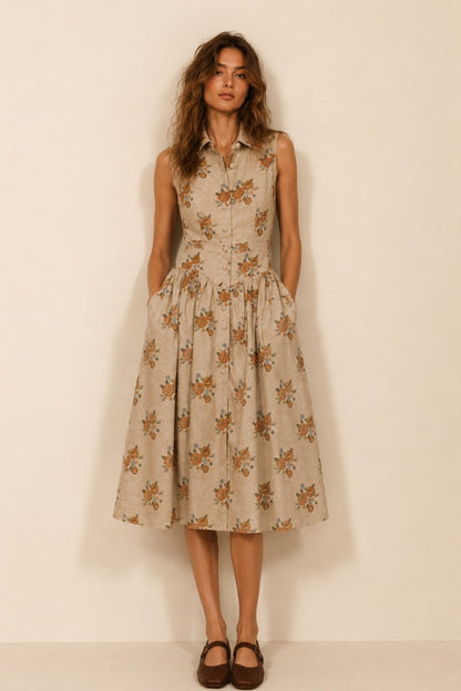 A women's sleeveless cream midi dress featuring a warm floral print, a collared neckline, front button closures, a gathered waistline, and functional side pockets.
