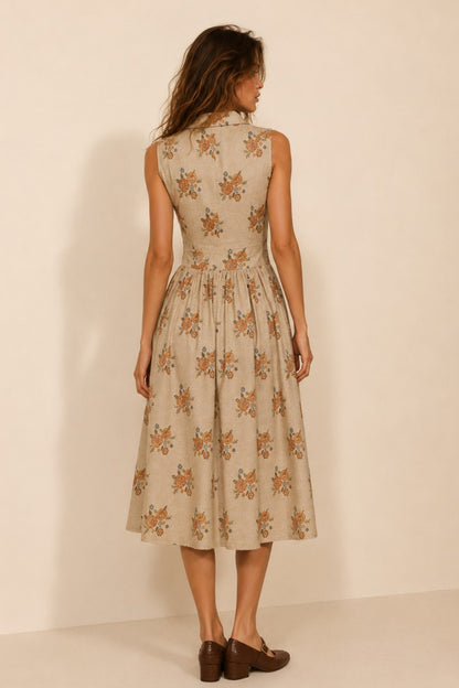 A women's sleeveless cream midi dress featuring a warm floral print, a collared neckline, front button closures, a gathered waistline, and functional side pockets.