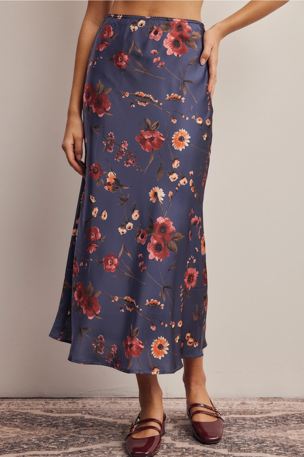 A women's bias-cut satin midi skirt in a midnight navy blue floral print featuring warm rust and amber blossoms with an elasticized waistband.