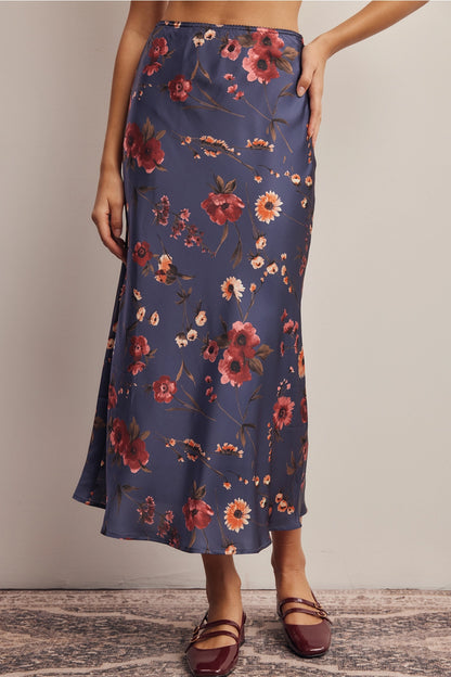 A women's bias-cut satin midi skirt in a midnight navy blue floral print featuring warm rust and amber blossoms with an elasticized waistband.