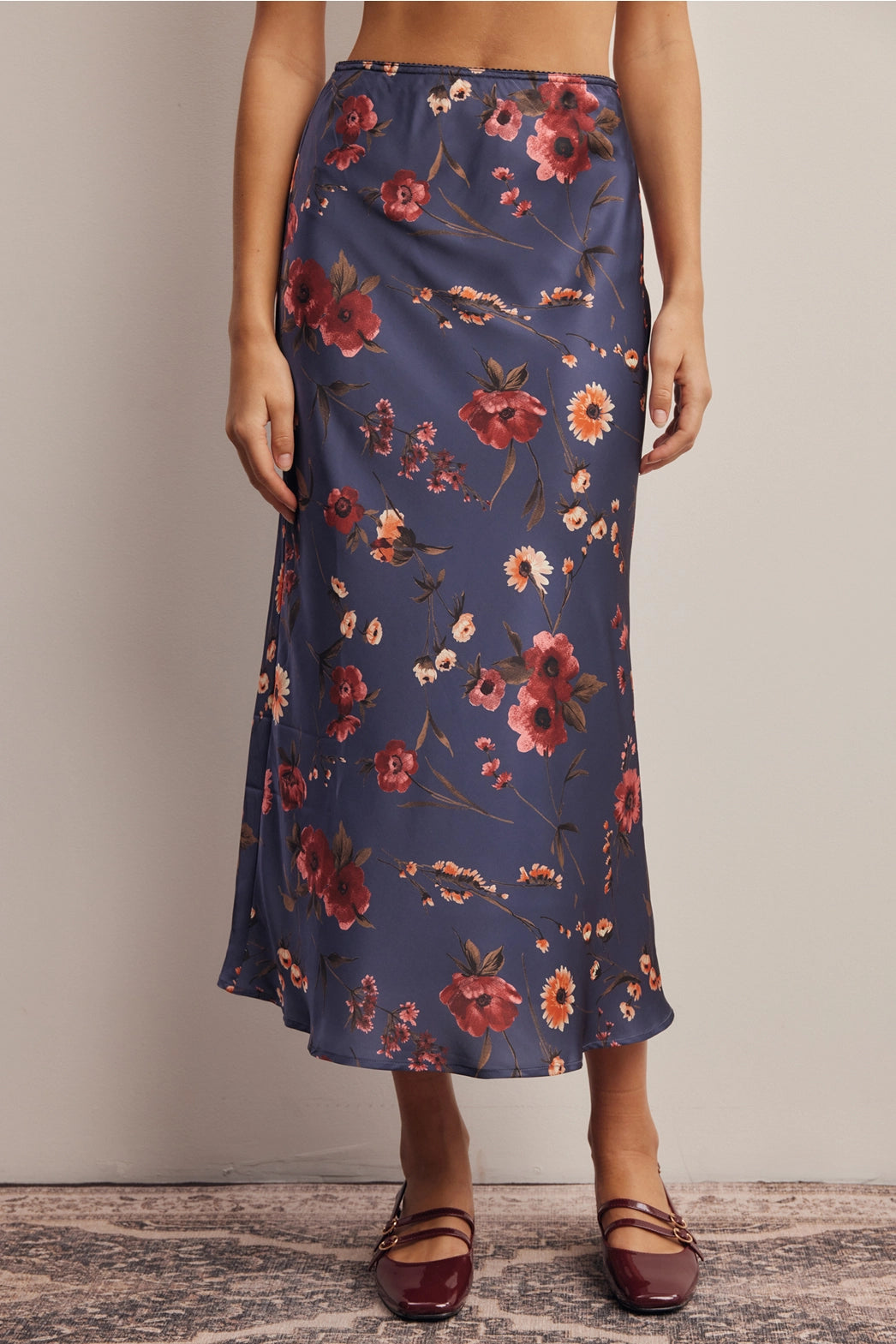 A women's bias-cut satin midi skirt in a midnight navy blue floral print featuring warm rust and amber blossoms with an elasticized waistband.