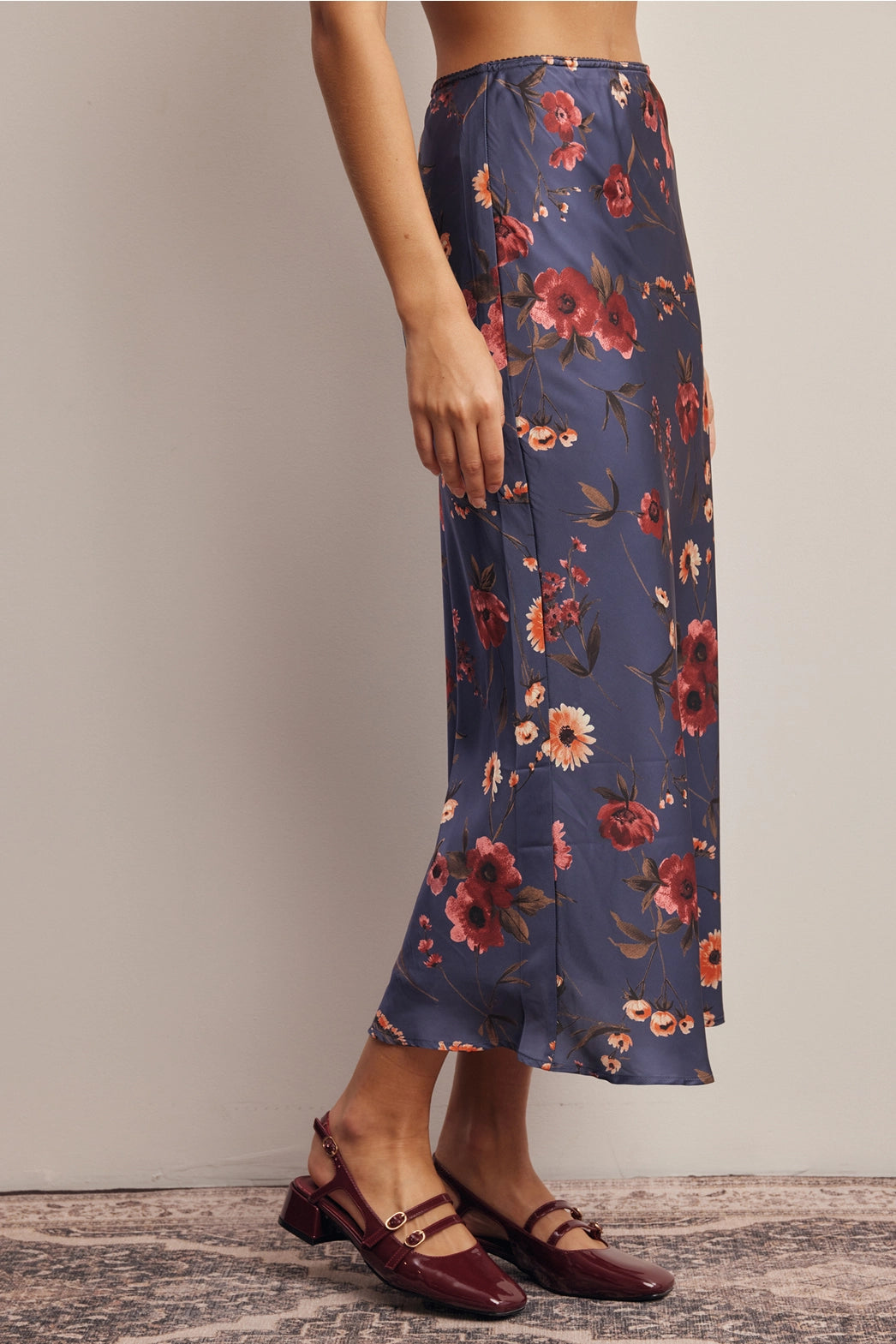 A women's bias-cut satin midi skirt in a midnight navy blue floral print featuring warm rust and amber blossoms with an elasticized waistband.