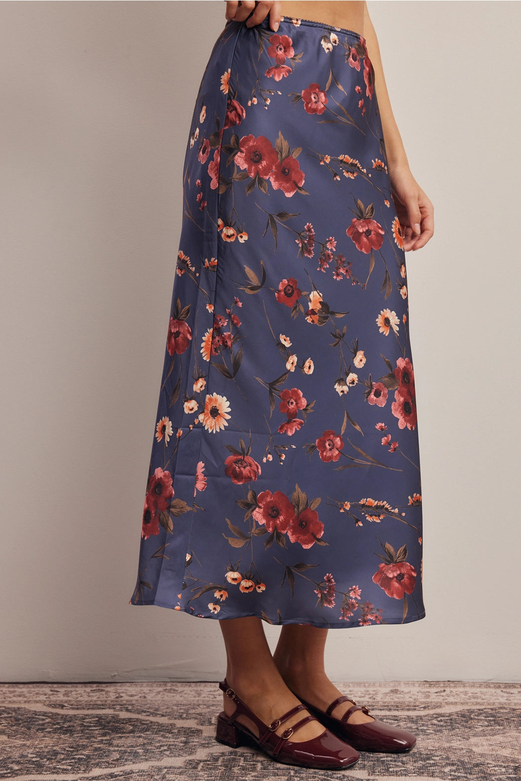 A women's bias-cut satin midi skirt in a midnight navy blue floral print featuring warm rust and amber blossoms with an elasticized waistband.