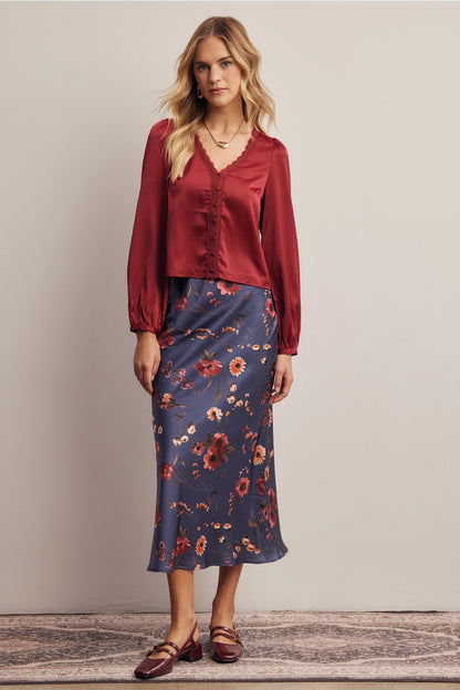 A women's bias-cut satin midi skirt in a midnight navy blue floral print featuring warm rust and amber blossoms with an elasticized waistband.