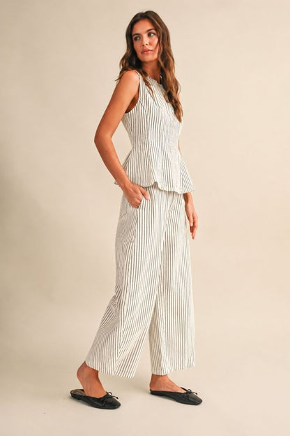 A women's two-piece matching set in a natural oatmeal and black pinstripe pattern featuring a sleeveless round-neck peplum top and relaxed wide barrel-leg pants paired with black flats.