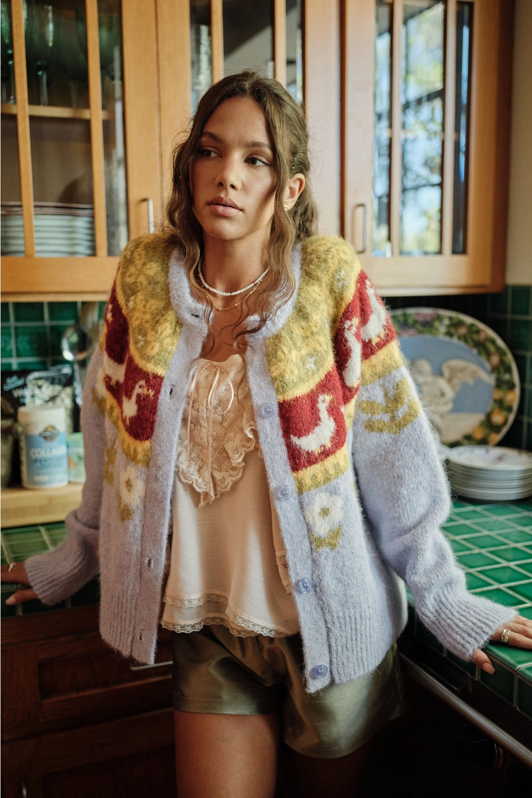 A women's soft lilac brushed knit button-down cardigan featuring a mustard yellow and burgundy Nordic yoke pattern with geese and floral garden motifs.