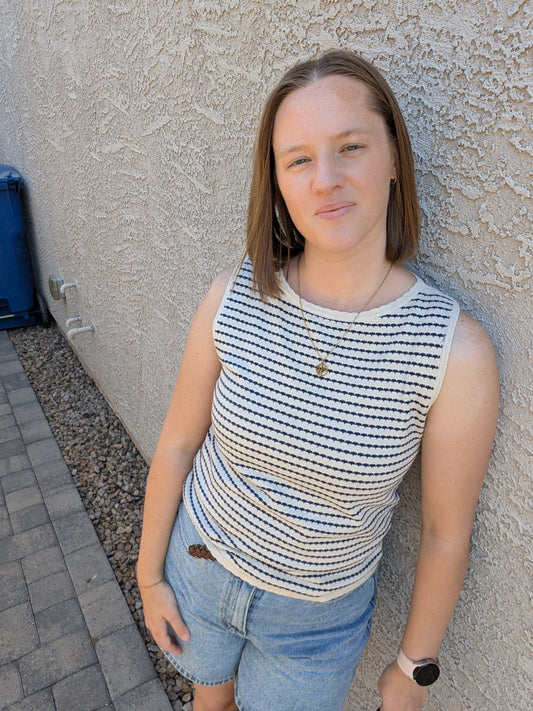 A sleeveless horizontal stripe knit sweater tank featuring a high boatneck, delicate ribbed trim at the hem and armholes, and a neutral oatmeal and navy color palette.