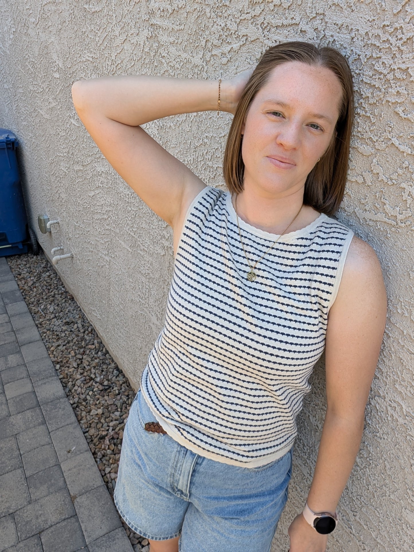 A sleeveless horizontal stripe knit sweater tank featuring a high boatneck, delicate ribbed trim at the hem and armholes, and a neutral oatmeal and navy color palette.