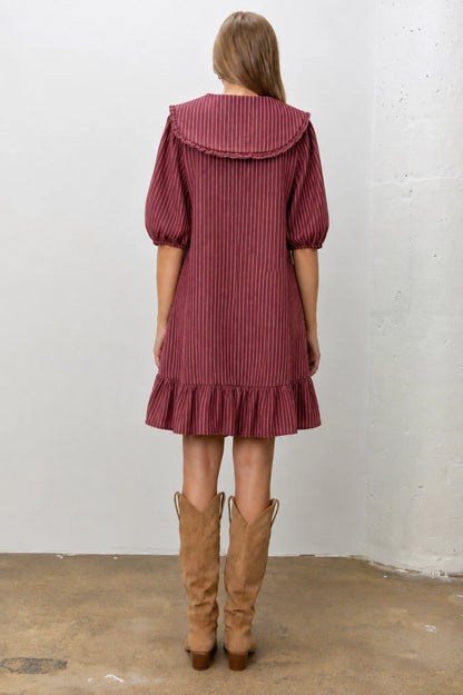 A women's relaxed short-sleeve shift dress in dark red and ivory striped denim featuring an oversized sailor collar with a tie neckline and a ruffled hem.