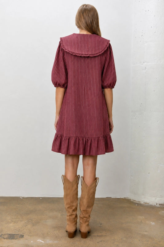 A women's relaxed short-sleeve shift dress in dark red and ivory striped denim featuring an oversized sailor collar with a tie neckline and a ruffled hem.