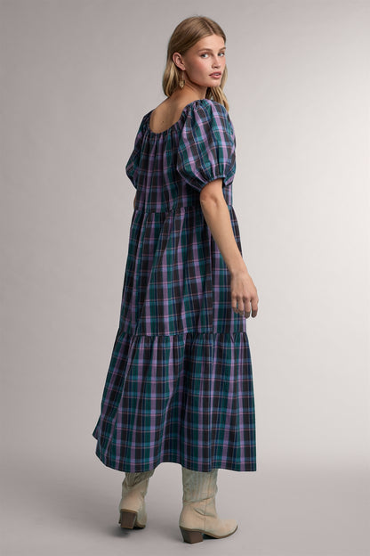 A women's tiered midi-length dress in a green and violet plaid pattern featuring short puff sleeves, a gathered scoop neck with a tie detail, and functional side pockets.