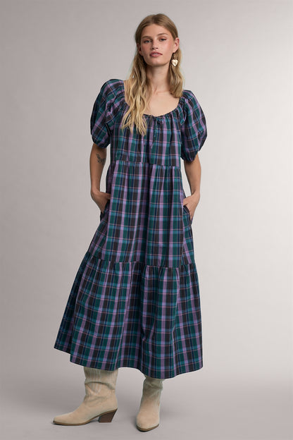 A women's tiered midi-length dress in a green and violet plaid pattern featuring short puff sleeves, a gathered scoop neck with a tie detail, and functional side pockets.