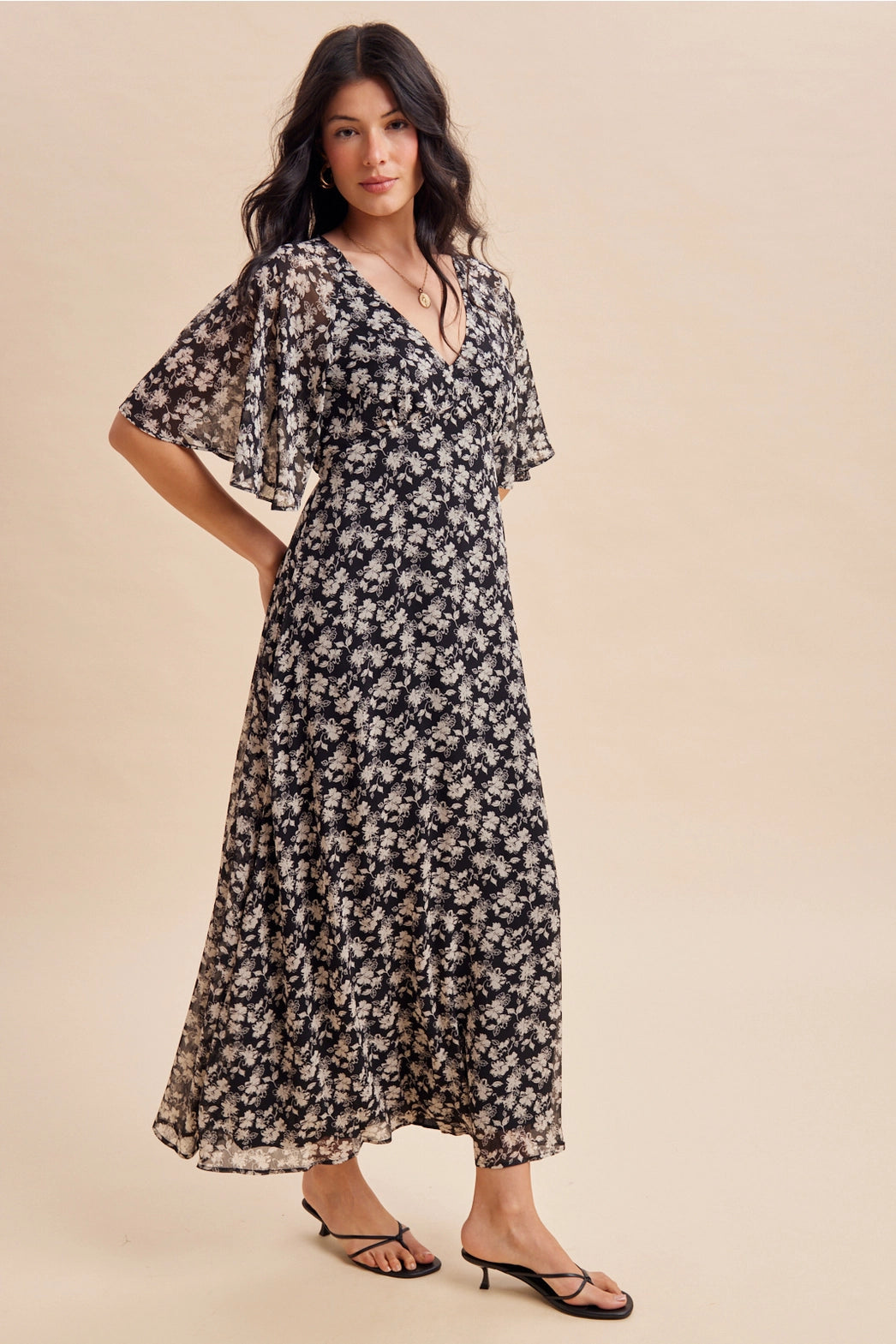A women's v-neck maxi dress in a black and cream floral print featuring short flutter sleeves and an empire waist silhouette.